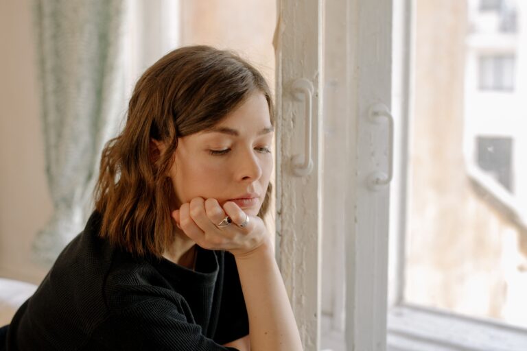 Mujer pensativa junto a una ventana reflexionando sobre el apego emocional en la pareja