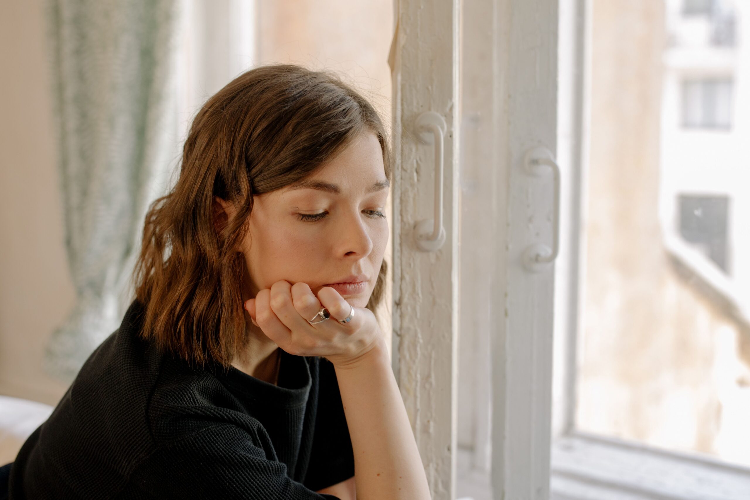 Mujer pensativa junto a una ventana reflexionando sobre el apego emocional en la pareja
